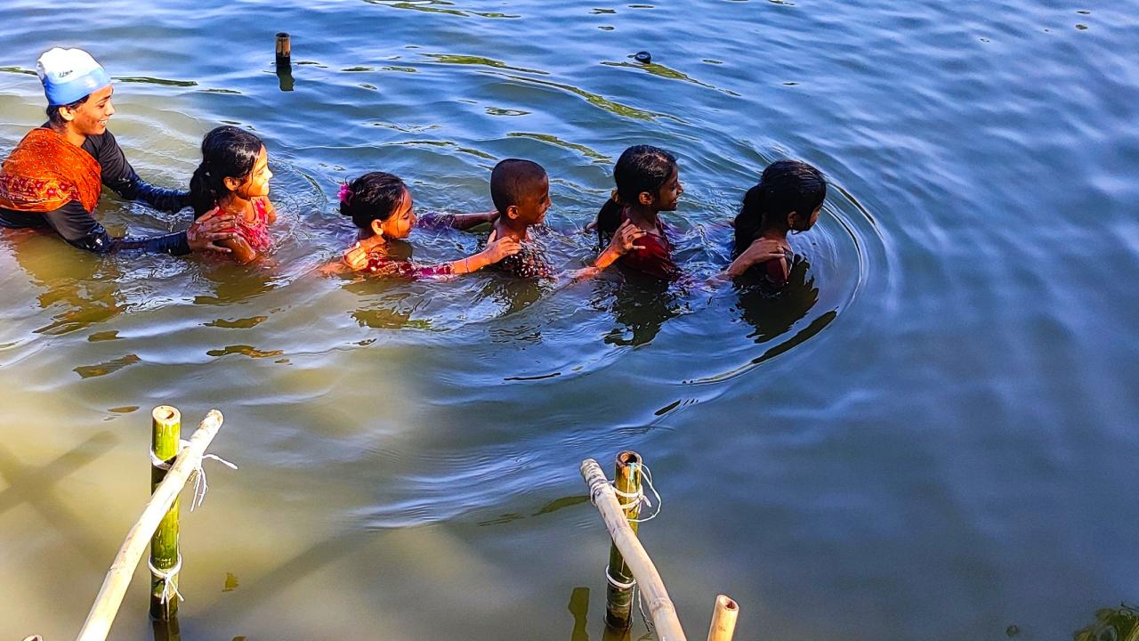 Children in a river being taught to swim