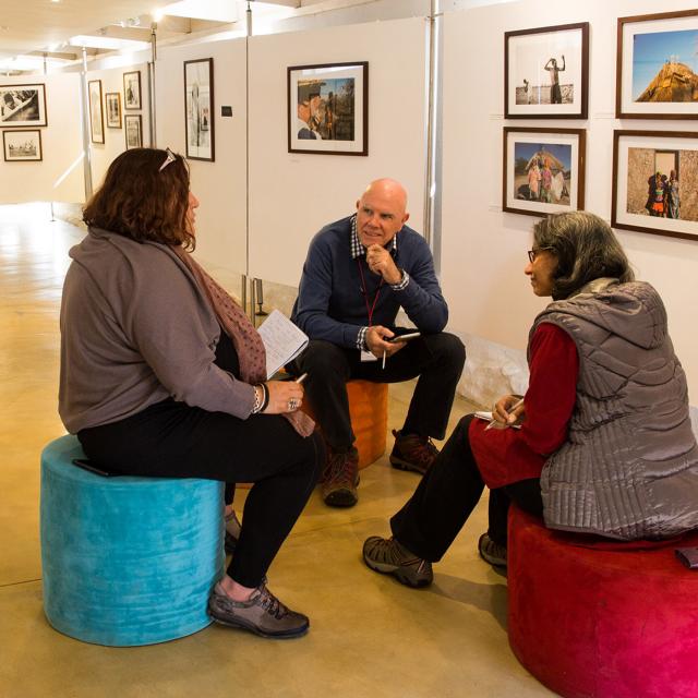 Three Synergos Senior Fellows sitting on chairs in an art space talking 